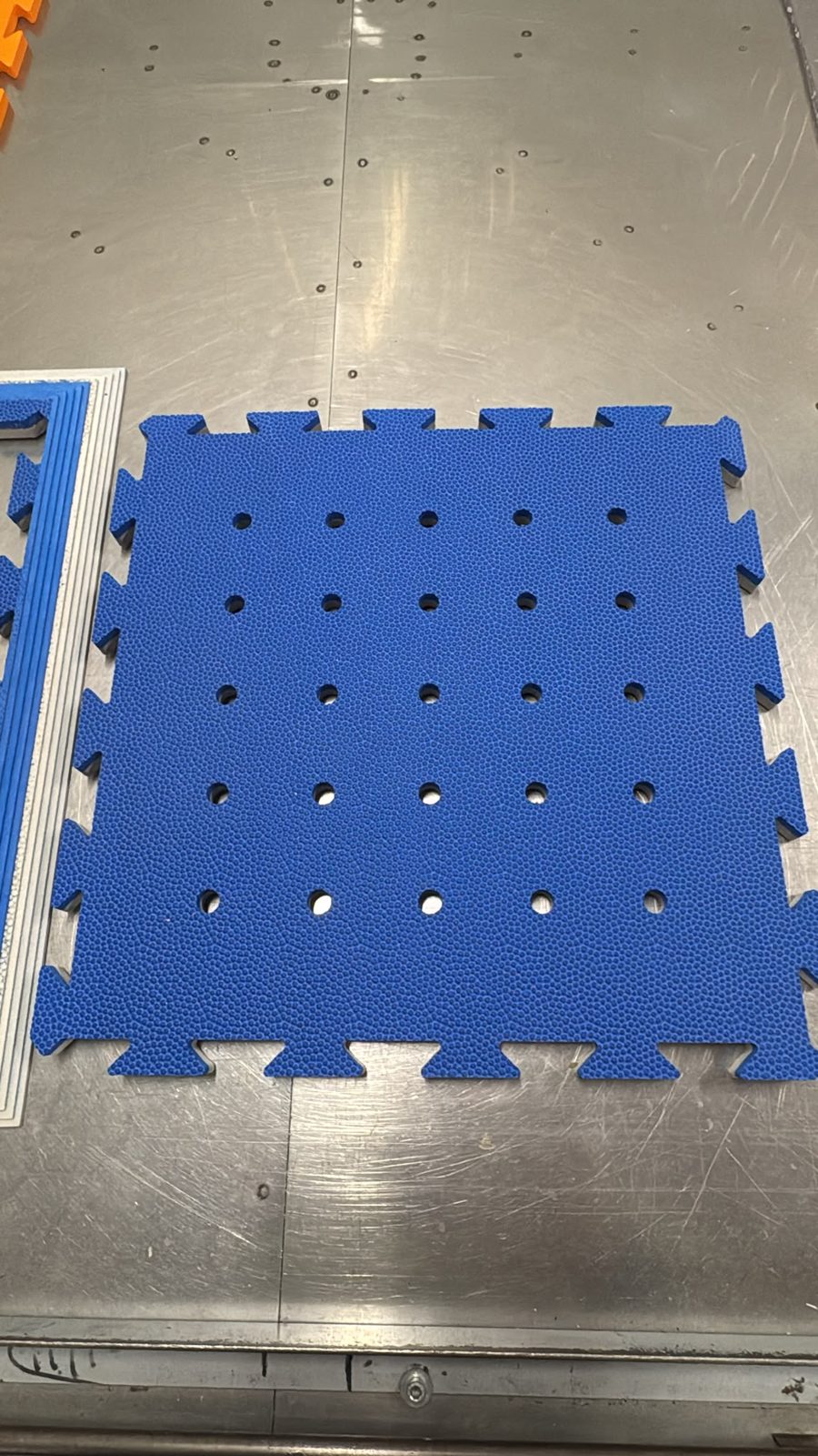 PORA-Puzzleteil aus dem Prototyp: blaue SAFEFLOOR-Oberfläche mit Wabenprägung, Verzahnung an allen vier Seiten und 5 × 5 Löchern
